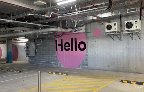 Pink 'Hello' mural in a parking garage with accessible parking signage.