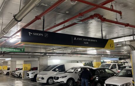 Underground parking lot with directional signage for shops and exits.