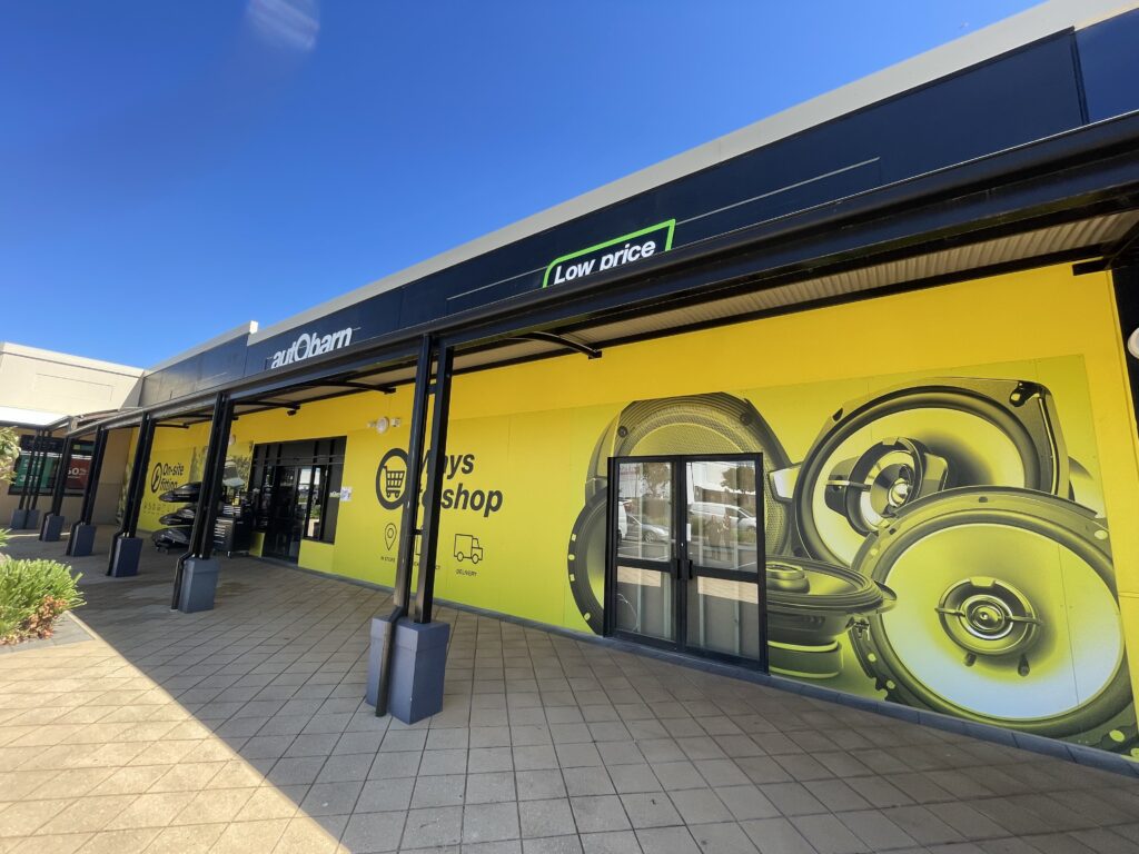 Autobarn shop signs storefront featuring a bright yellow mural with speaker graphics.