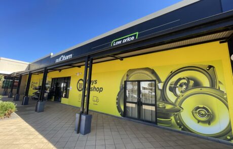 Autobarn shop signs storefront featuring a bright yellow mural with speaker graphics.