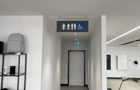Hanging restroom signage with accessibility symbols in a modern office