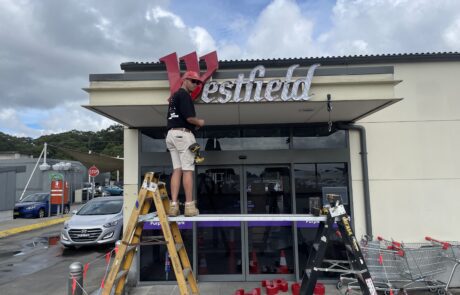 Worker on a ladder performing maintenance on Westfield signage.