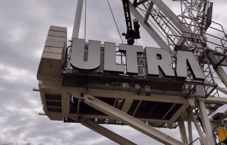 Large “ULTRA” signage being installed on a crane platform against a cloudy sky.